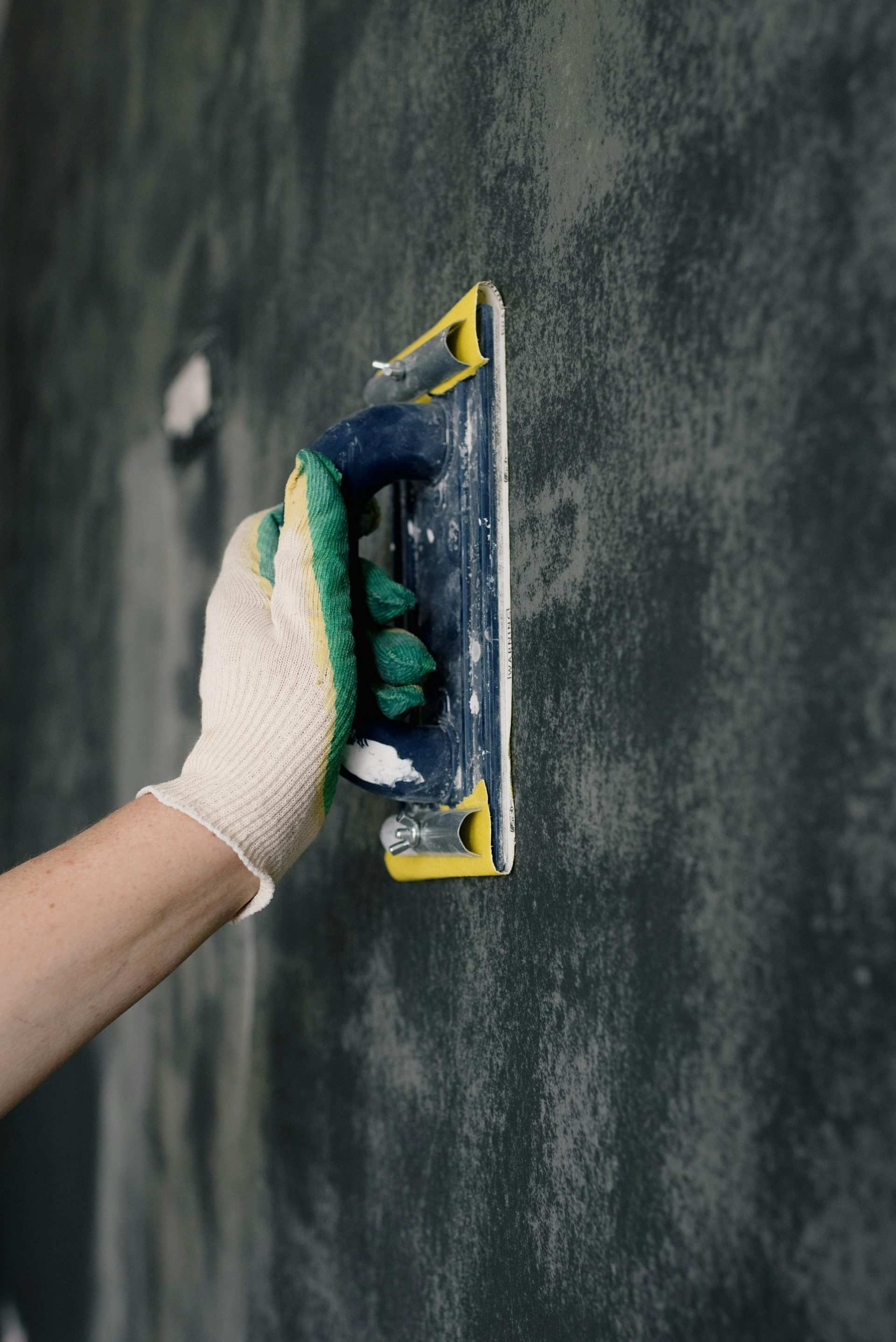 Anonymer männlicher Arbeiter in Handschuhen hält Schaber und richtet Wände in Wohnung aus