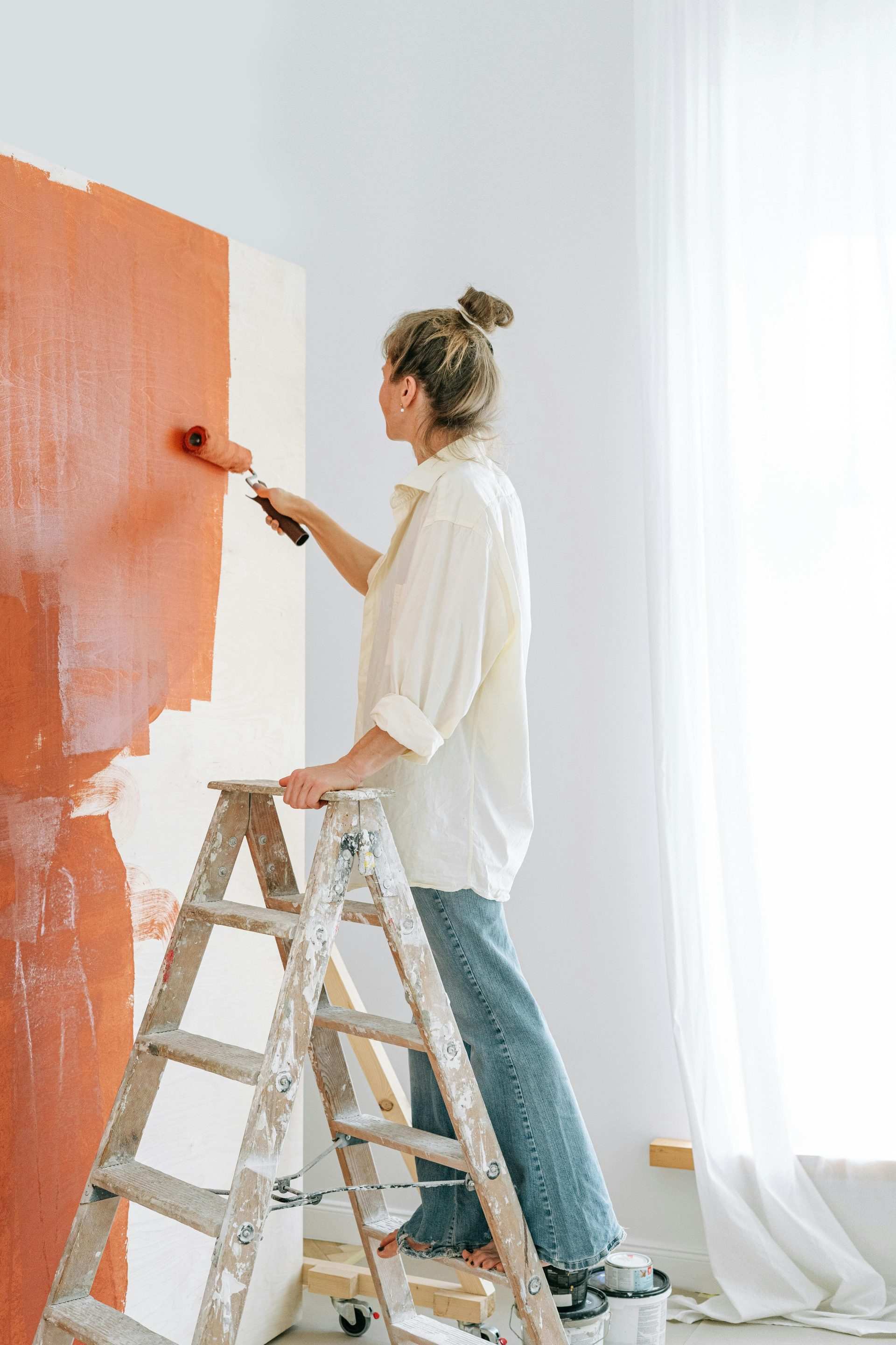 A woman uses a paint roller to apply gray paint on a wall during a home renovation project indoors.